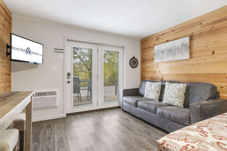 Interior Room With Wooden Walls, Gray Sofa, And Sliding Door To Balcony