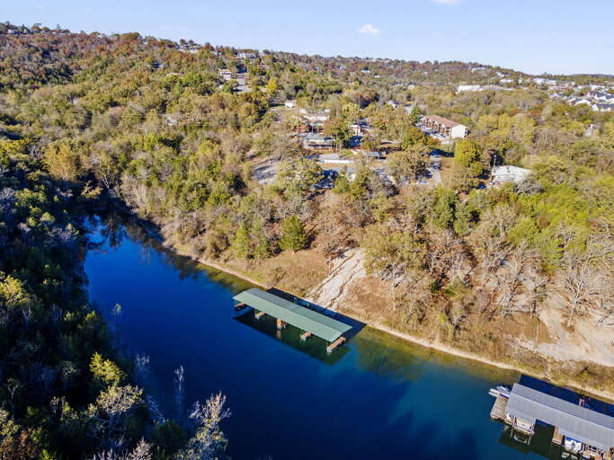 Aerial View Of A Serene Riverside Setting Surrounded By Verdant Vegetation With Floating Docks Visible