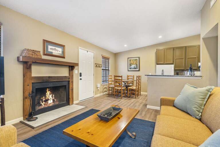 Living Room With Lit Fireplace, Kitchen Bar, Sofa, And Wooden Floor