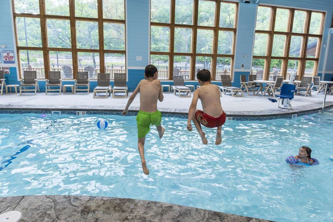 Boys Bounding Into Blue Pool, Bright Backdrop Of Big Windows