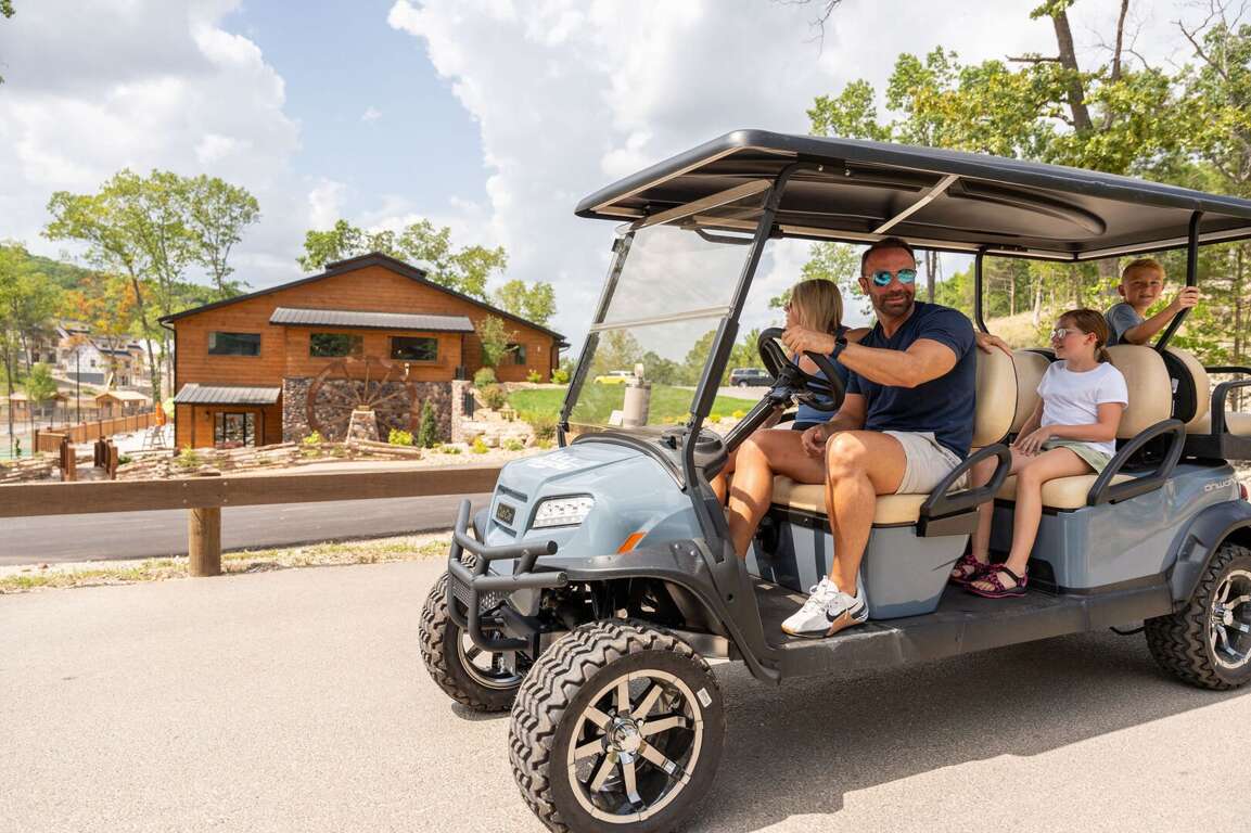 Family Riding Golf Cart Near Rustic Building