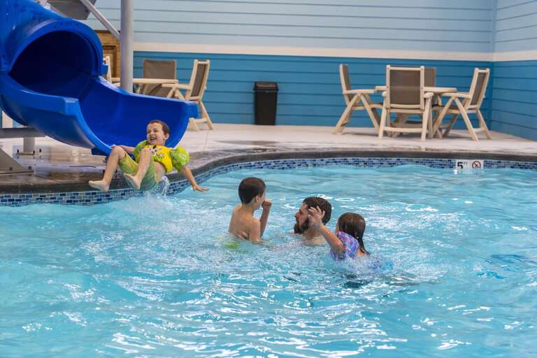 Family Frolicking In A Vacation Rentals Indoor Pool, Child Descending Slide