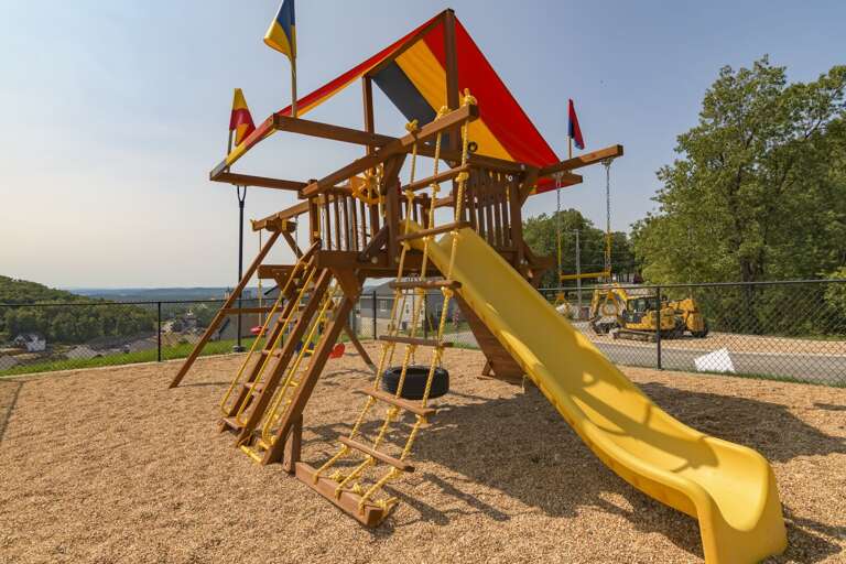 Wooden Playground Structure With Slides And Flags Under Sunny Skies