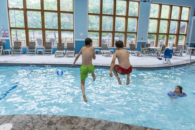 Boys Bounding Into Blue Pool, Bystanders Bask By Big Windows