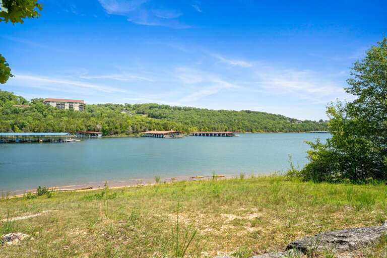 Lush Lakeside Landscape With Serene Sky And Distant Dwelling