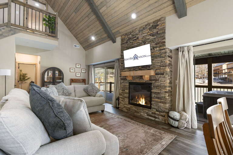 Spacious Living Area With Stone Fireplace And Vaulted Ceiling, Featuring Plush Sofas And Mounted TV