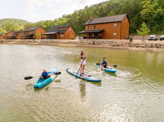 Lakeside Leisure, Paddling On Placid Waters, Rustic Buildings Backdrop