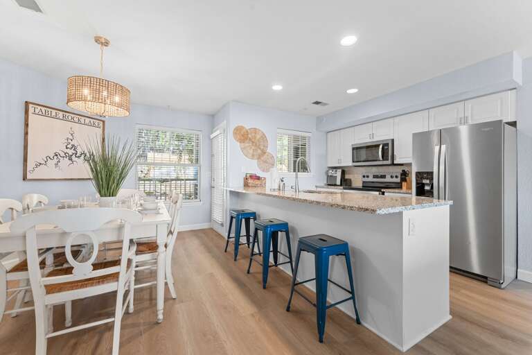 Spacious Kitchen With Bright Dining Area, Stainless Steel Appliances, And Blue Bar Stools