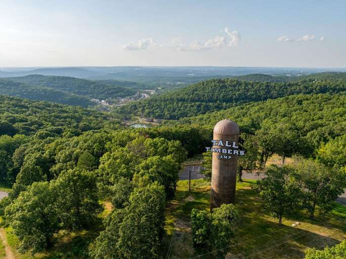 Aerial View Of A Large Water Tower Labeled STALLION SPRINGS Amidst Lush Greenery, Under Vast Vistas