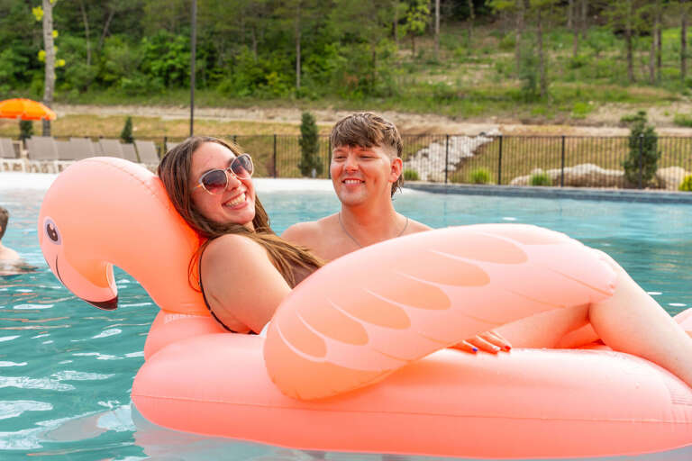 Pair Playfully Posed On Pink Flamingo Float In Pool