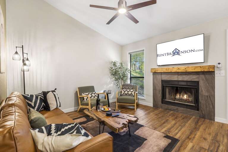 Living Room With Leather Sofa, Lit Fireplace, And Mounted Television