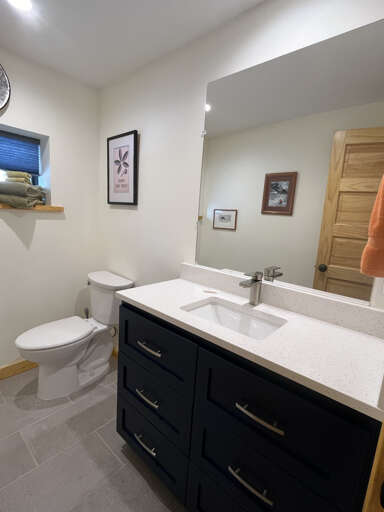 A crisp, modern bathroom awaits you with sleek navy cabinetry, gleaming white countertops, and thoughtful touches like fresh towels ready for your stay.