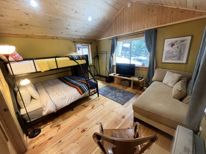 Your cozy cabin retreat features rustic wood walls, bunk beds, and a comfortable sofa for relaxing after mountain adventures.