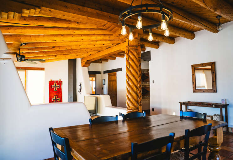 Gather around this handcrafted wooden dining table beneath rustic timber beams and warm lighting for memorable meals with loved ones.