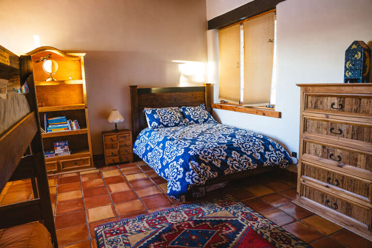 Relax in this charming bedroom with rustic wood furniture, colorful textiles, and warm lighting creating your perfect retreat.