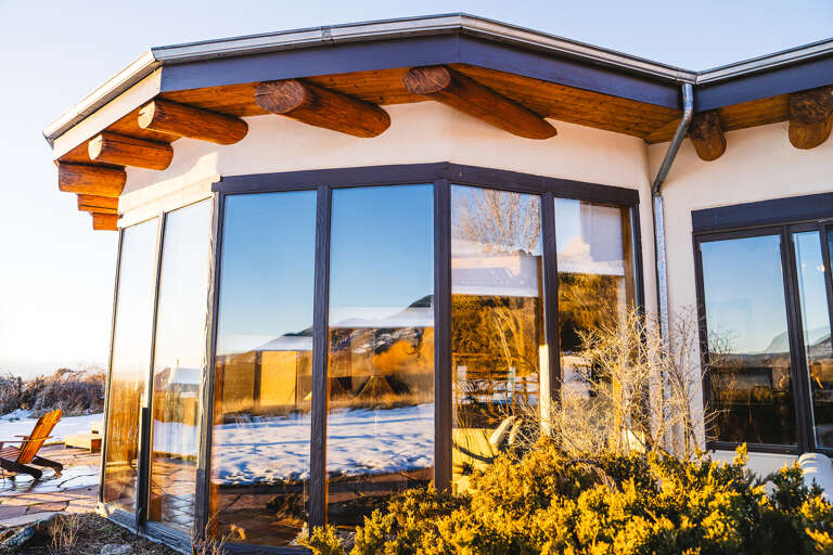 Modern property featuring distinctive architectural design with exposed wooden beams and expansive floor-to-ceiling windows overlooking snowy mountain landscape.