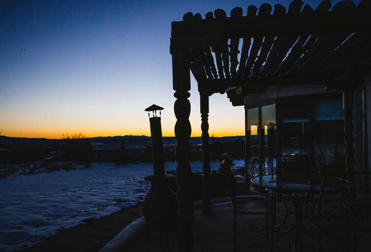 Property's covered patio overlooks snow-covered landscape at sunset, offering peaceful mountain views and outdoor seating area.