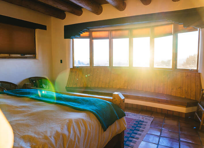 Wake up to golden sunlight streaming through expansive windows in your cozy bedroom, where rustic beams meet modern comfort.