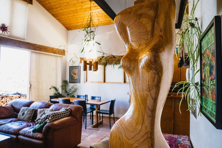 Unwind in your artistic living space featuring handcrafted wooden sculptures, cozy seating, and abundant greenery creating a unique, gallery-like atmosphere.