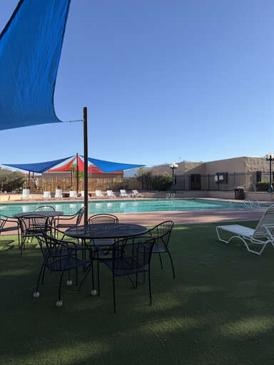The property features an outdoor pool and hot tub area with comfortable lounge chairs and shaded seating under colorful canopies, surrounded by arid mountains visible in the distance.