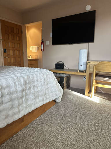 Unwind in your cozy bedroom with plush bedding, large wall-mounted TV, and thoughtful workspace setup for ultimate comfort and convenience.