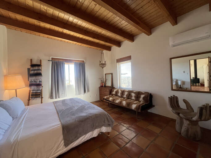 Relax in your rustic-chic bedroom featuring exposed wood beams, terracotta tiles, and stylish leather seating area.