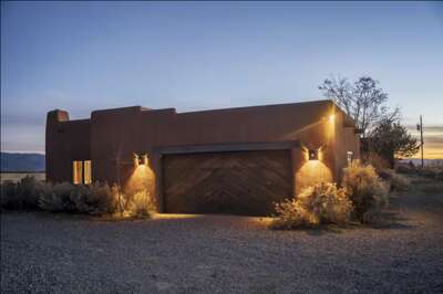 Adobe-style desert home with warm exterior lighting, nestled in a natural landscape with mountain views and serene sunlit skiesâyour Southwest retreat awaits.