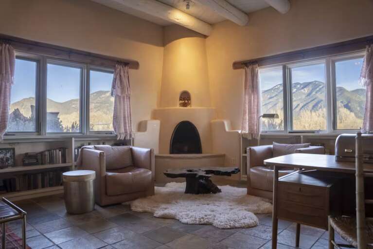Sink into plush seating by the kiva fireplace while your eyes drink in mountain vistas through expansive windows. This sun-drenched living space with exposed beam ceilings invites you to unwind in Southwestern elegance.