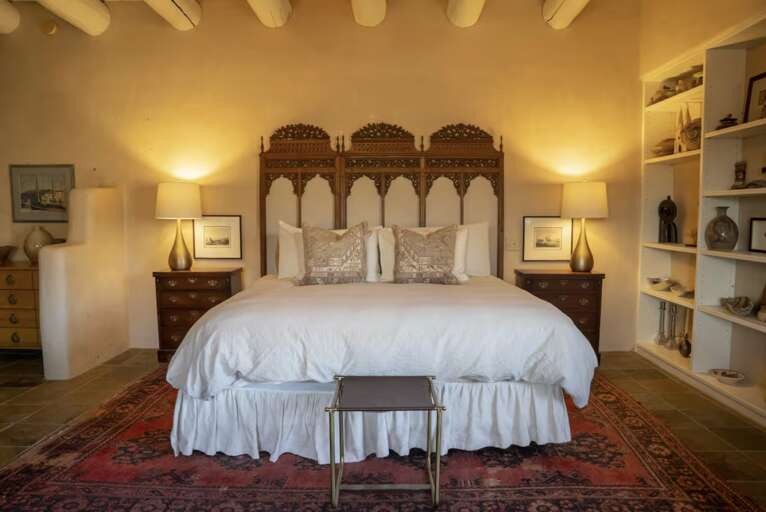 Sink into plush white linens beneath an intricately carved headboard, where warm lamplight and authentic architectural details create your peaceful sanctuary.
