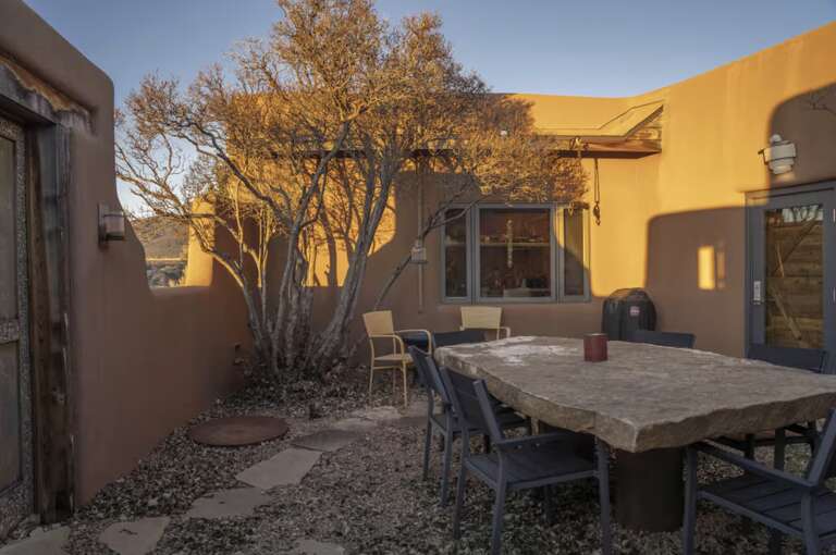 Warm adobe walls surround a serene courtyard with a stone dining table, perfect for outdoor meals beneath autumn trees as golden hour light creates a peaceful desert ambiance.