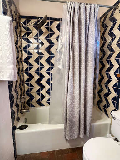 Step into your private bathroom featuring a striking geometric tile pattern and a refreshing tub-shower combo, complete with plush towels waiting for you.