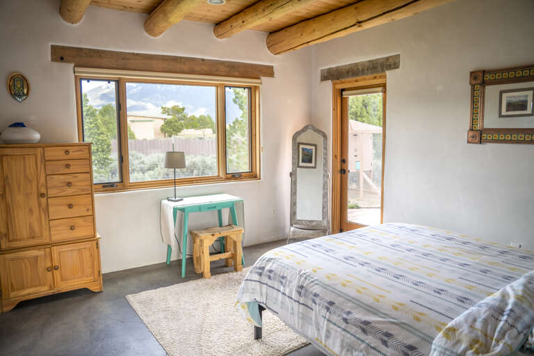 Drift off in your bright bedroom with authentic viga ceilings and a private door to your outdoor space. Natural light floods in through large windows framing garden views, while handcrafted wood furnishings add Southwest charm.