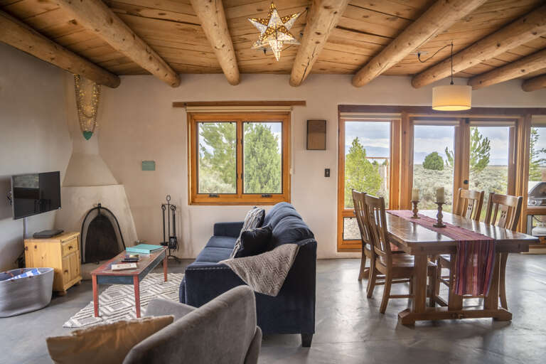 Relax under dramatic wooden beam ceilings in your open-concept living and dining space, where large windows frame sweeping natural landscape views and a cozy fireplace invites you to unwind.