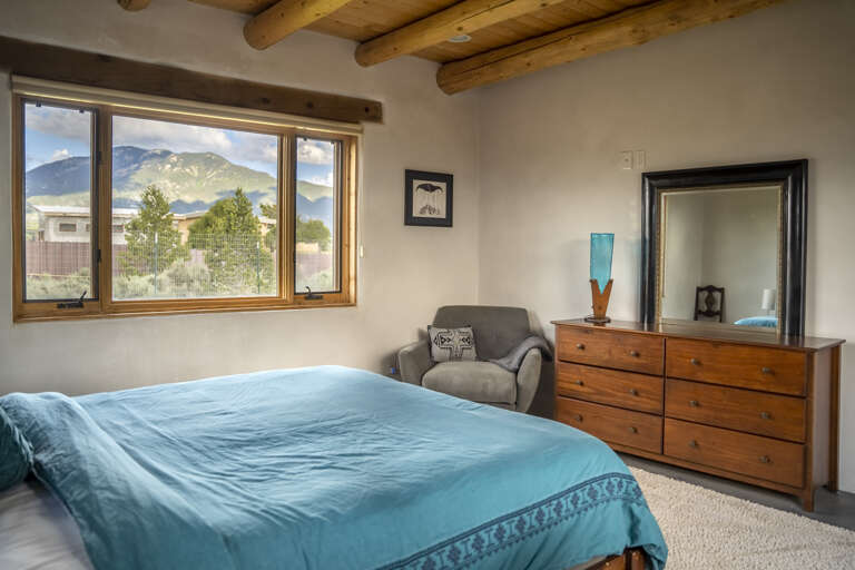 Wake up to stunning mountain views framing your window in this serene bedroom, where exposed beam ceilings and warm wood accents create a cozy southwestern retreat for your perfect mountain getaway.