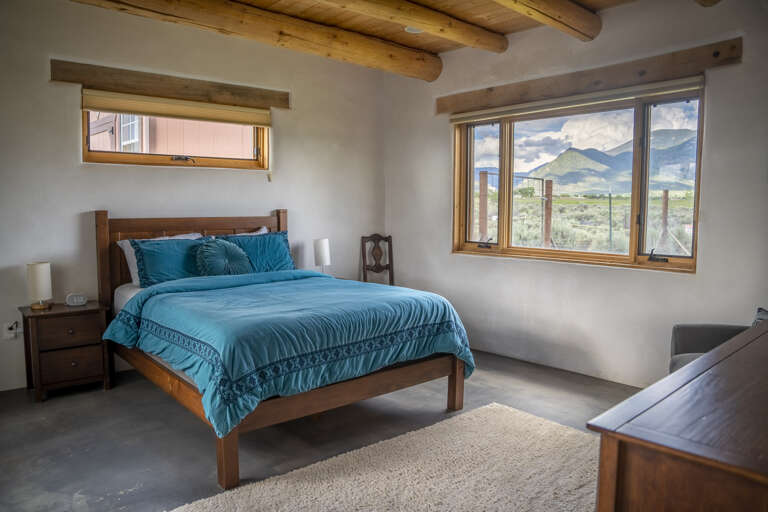 Wake up to sweeping mountain vistas from your serene bedroom, where rustic wood beams overhead and turquoise bedding create the perfect blend of comfort and natural beauty.