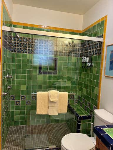 Step into your private bathroom featuring vibrant hand-painted tiles in emerald green and gold, complemented by intricate decorative accents and plush towels waiting for you.
