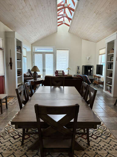 Gather around the dining table or relax in the living room beneath soaring wood-planked ceilings and a stunning skylight. Natural light fills the space, inviting you to unwind and feel right at home.