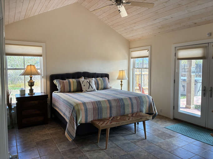 Step into your peaceful retreat with vaulted wood ceilings and French doors opening to your private outdoor space. The coastal-inspired bedding invites restful nights while natural light pours through generous windows.