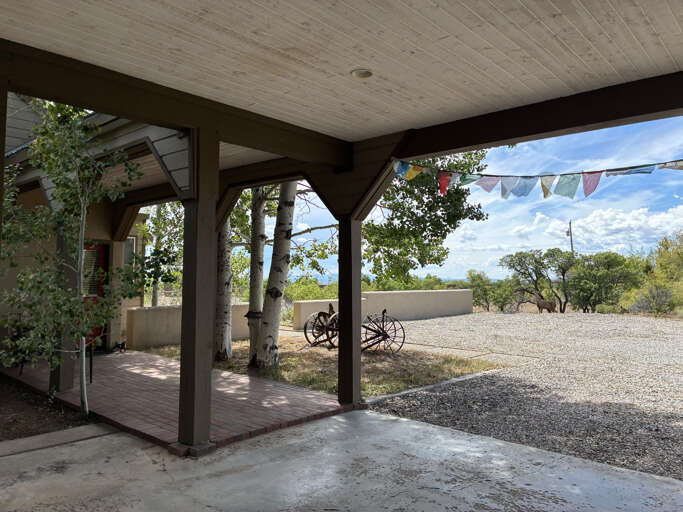 A welcoming covered patio opening to scenic natural surroundings with mountain vistas, mature trees, and ample parking for a stress-free arrival at your peaceful retreat.