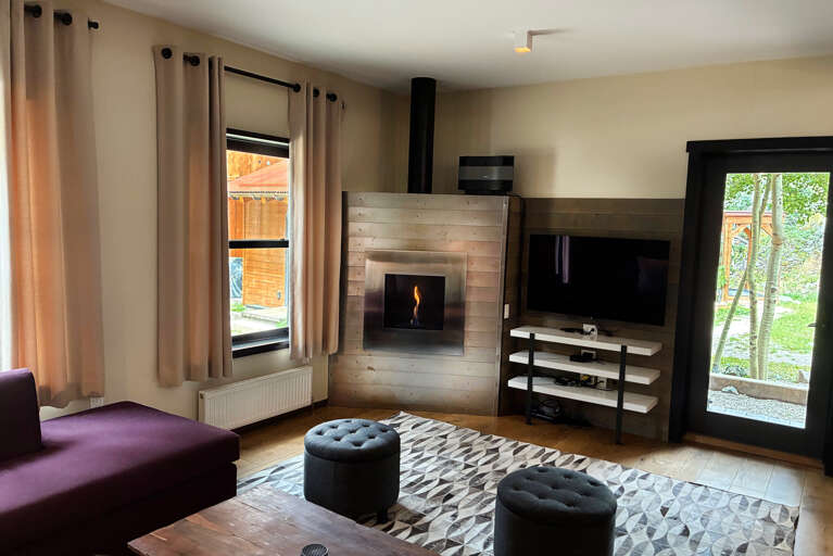 Cozy up in your stylish living room with a warm fireplace, flat-screen TV, and natural light streaming through large windows overlooking the garden. Perfect for relaxing after a day of adventure.
