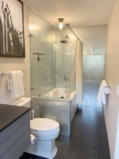 Unwind in your sleek modern bathroom with a spacious glass-enclosed tub and rainfall shower. Crisp white towels await, and the polished tile creates a spa-like escape.