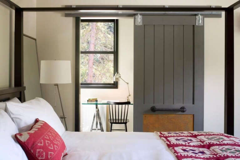 Sink into crisp white linens in your charming bedroom, where rustic elegance meets modern comfort. A sliding barn door leads to your work nook, and natural light frames peaceful forest views.