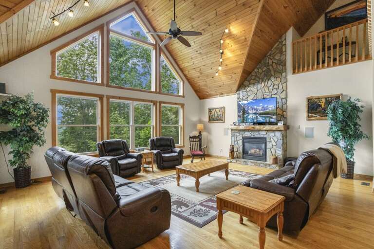 Wildlife Manor Living Room with a Wall of Windows, Stacked Stone Gas Fireplace and Leather Furniture