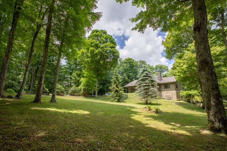 House sits on a very large yard with lots of grass and mature trees