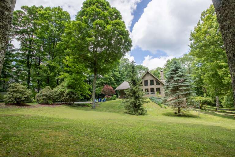 House sits on a very large yard with lots of grass and mature trees
