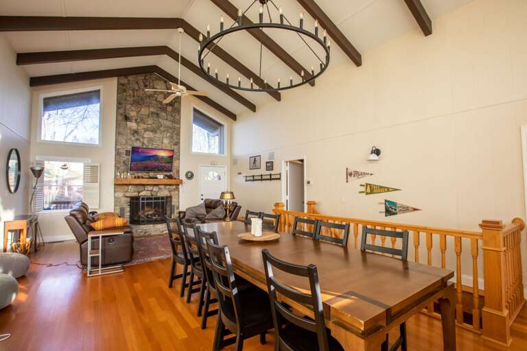 Spacious Interior Showing Stone Fireplace, Wooden Dining Set, And High Ceilings