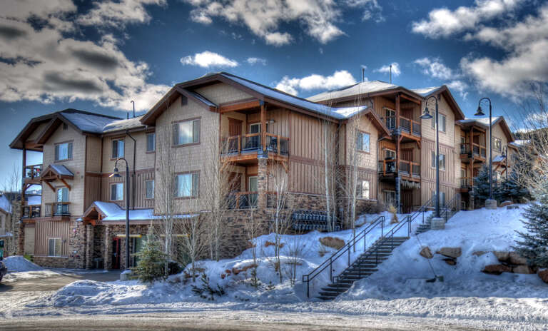 Mountain lodge nestled in a snowy setting, featuring stone and wood architecture with private balconies under blue winter skies.