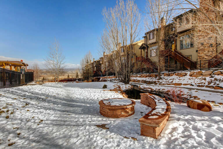 A snow-dusted backyard showcasing mountain views, a fire pit, and curved seating—perfect for winter gatherings under clear blue skies.