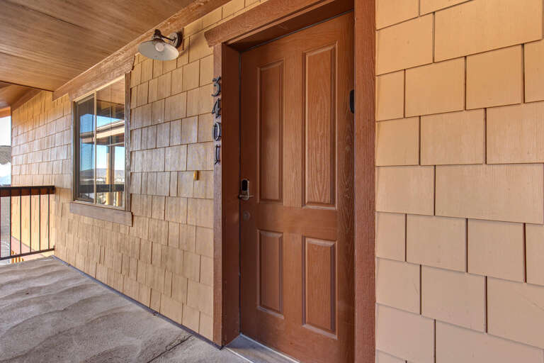 The entrance presents natural wood shingle siding and a warm wooden door, marking your arrival at this mountain retreat with rustic charm.