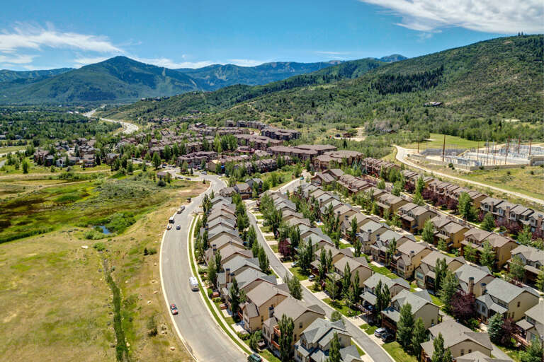 Aerial view showcasing a scenic mountain valley with forested slopes and residential neighborhoods nestled in the surrounding natural landscape.